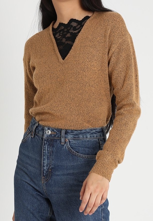 Maglione marrone a maglia con scollo a V e maniche lunghe, sovrapposto a un top in pizzo nero. Caratterizzato da un tessuto strutturato e una vestibilità rilassata. Indossato con jeans blu a vita alta.