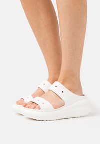 Bele platform sandale z dvema širokima trakoma in okroglimi izrezi. Gladka tekstura in zaobljena zasnova, ki prikazuje minimalistični slog.
