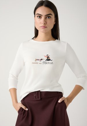 Weißes Langarmshirt mit einem grafischen Design, das den Text "Cuddle me BONJOUR" zeigt, kombiniert mit dunkelburgunderfarbenen, hoch taillierten Hosen.