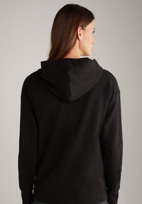 Felpa nera con una texture liscia, dotata di cappuccio, maniche lunghe e un discreto dettaglio del logo sulla manica. Design semplice e funzionale.