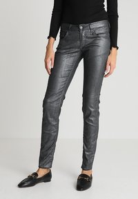 Jean skinny gris métal avec une légère brillance, cinq poches, passants de ceinture et fermeture éclair, associés à des mocassins noirs.