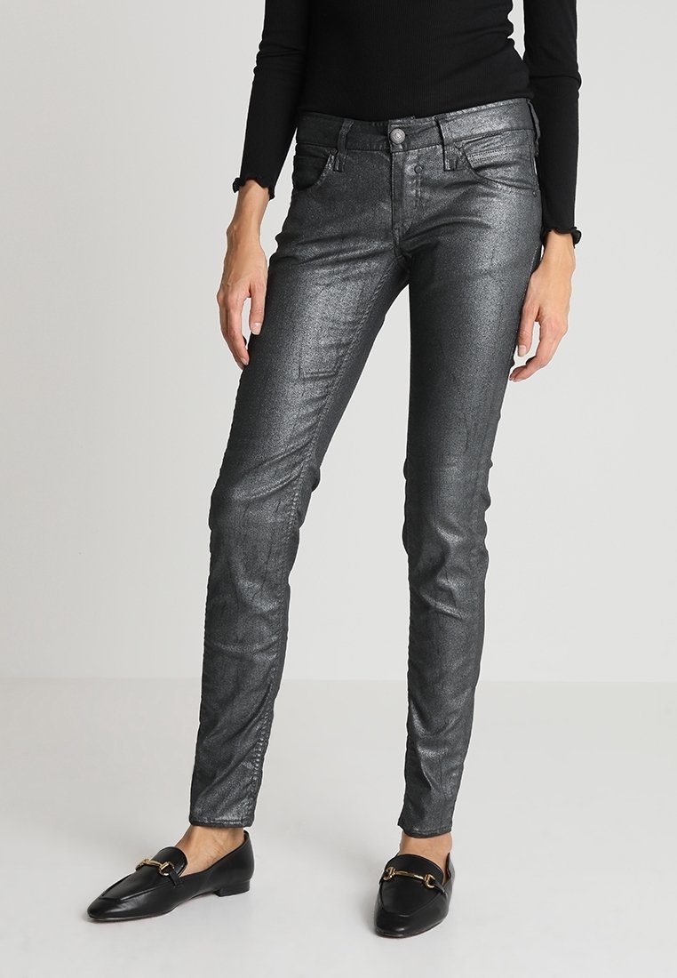 Jean skinny gris métal avec une légère brillance, cinq poches, passants de ceinture et fermeture éclair, associés à des mocassins noirs.