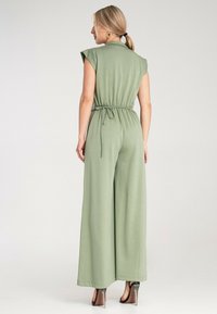 Zielony kombinezon z rękawami typu cap, talią wciętą i szerokimi nogawkami. Wykonany z miękkiego materiału o gładkiej teksturze. Minimalistyczny design.