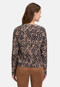 T-shirt à manches longues en tissu texturé, présentant un imprimé léopard marron et beige sur fond sombre, avec un col rond et un ourlet droit.