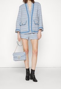 Blå och vit mönstrad tweedblazer med V-ringning, tillsammans med matchande shorts. Svarta ankelskiner och en blå väska med kedjestropp.