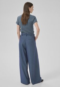 Blau gestreiftes T-Shirt kombiniert mit weit geschnittenen, gestreiften Hosen in einem dunkleren Blau. Die Hose hat einen Gürtel und Gesäßtaschen sowie eine glatte Textur.