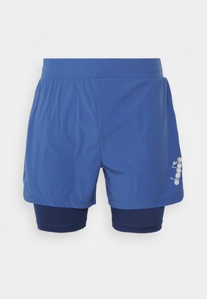 Niebieskie warstwowe męskie sportowe szorty z elastycznym paskiem w talii i białym logo na prawej nodze na jednolitym szarym tle.