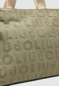 Torebka w oliwkowym kolorze z wypukłymi, teksturowanymi literami tworzącymi powtarzający się wzór "JOLI". Uchwyty wykonane są z plecionego materiału.