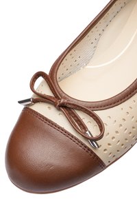 Detailní záběr dámské béžové baleríny s hnědou špičkou, perforovanými boky a dekorativní hnědou mašlí s kovovými konci.