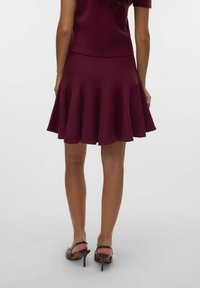 Jupe plissée bordeaux avec une taille cintrée, fabriquée en tissu texturé, associée à des chaussures à talons violettes assorties.