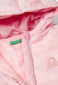 Růžová péřová bunda s měkkou vnitřní podšívkou, zipovým zapínáním a vyšívaným logem. Obsahuje kapuci a prošívaný vzor po celém povrchu.