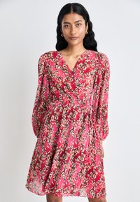 Pink floral wrap dress with long sleeves, made of lightweight fabric, featuring a gathered waist and flowing skirt.
