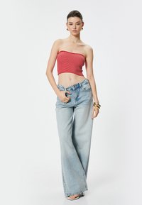 Top corto a righe rosse e jeans a gamba larga blu chiaro. I jeans presentano un'alta vita e un classico design a cinque tasche. Texture liscia.
