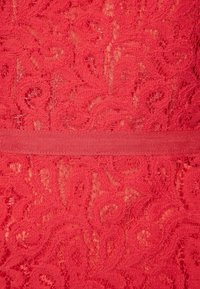 Röd spets tyg med ett svängande blommönster och en slät textur. Ett matchande rött elastiskt band syns vid midjan.