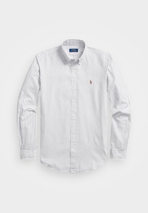Chemise à rayures blanches et bleu clair, avec des manches longues, un col et un petit logo brodé sur la poitrine. Texture en coton lisse.
