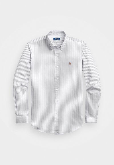 Balts un gaiši zils svītrainais krekliņš ar garām piedurknēm, apkakli un mazu izšūtu logo uz krūtīm. Gluda kokvilnas tekstūra.