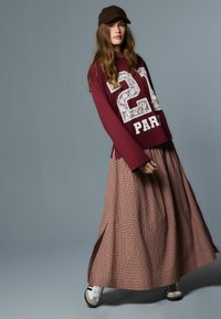 Tumesinine pika varrukaga särk, millel on tekst "27 PARIS", koos pruuni ruudulise seelikuga. Komplementaarsete aksessuaaridena pruun nokats ja valged tossud.