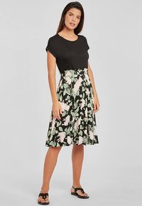 Juoda palaidinė derinama su gėlėtu sijonu, kuriame juodas fonas, baltos ir žalios gėlės bei prigludusi elastinė liemens juosta.