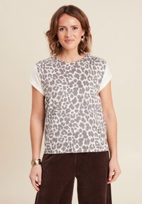 Luipaardprint top met korte mouwen, met een lichtgekleurde basis en grijze vlekken. Draagt met een bruine corduroy broek. Gestructureerd materiaal.
