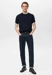 Námořnický crew-neck tričko, tmavé džíny s ohrnutými manžetami, černý opasek a černé šněrovací boty. Jednoduchý, moderní design s ležérním střihem.
