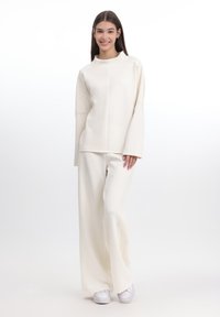 Set composto da un top a maniche lunghe di colore crema e pantaloni larghi. Materiale morbido con dettagli testurizzati sulle maniche e sui pantaloni, abbinato a sneaker bianche.