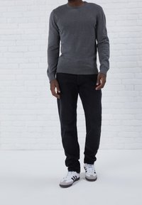 Szary pulower z długim rękawem i okrągłym dekoltem, wykonany z miękkiego materiału, w zestawieniu z ciemnymi dżinsami i białymi trampkami z czarnymi i szarymi akcentami.