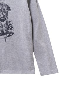 Graues Langarmshirt mit einem schwarzen Grafikdruck eines Hundes, der ein Trikot trägt. Der Stoff wirkt weich mit einer glatten Textur.