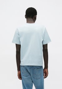 Jasnoniebieski bawełniany t-shirt z krótkimi rękawami i okrągłym dekoltem, zestawiony z niebieskimi dżinsami, widziany od tyłu. Prosty wzór.