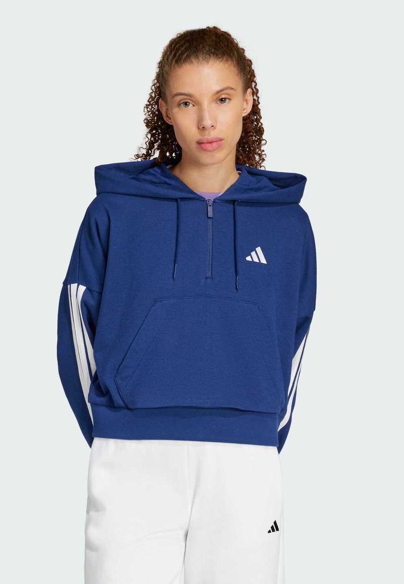 Plava dukserica od mekanog materijala, s polu-zatvaračem, prednjim džepom i bijelim prugama na rukavima. Adidas logo na prsima.