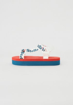 Platte sandalen met een rode schuimbasis en blauwe zool, met witte banden bedrukt met 'Stella'. Gladde textuur en modern design.