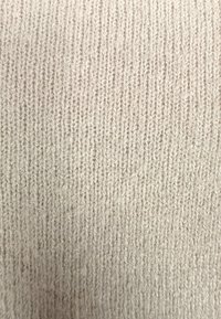 Jasnobeżowa dzianina o drobnej, pionowej fakturze prążkowania. Materiał wydaje się miękki, z subtelnymi różnicami w głębokości i lekko puszystą powierzchnią.