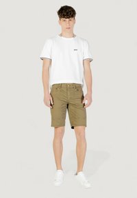 T-shirt bianco con logo nero e colletto a costine, abbinato a pantaloni cargo verde oliva. Il modello indossa sneakers bianche.