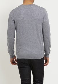 Gray knit sweater with long sleeves, round neckline, and ribbed cuffs. Material appears soft and smooth, layered over dark denim pants.