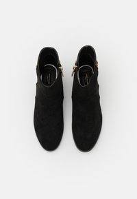 Botines de ante negro con un diseño curvado, que presentan una silueta ajustada, cremalleras doradas y un acabado texturizado en la parte superior.
