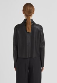 Schwarze Lederjacke mit einer verkürzten Passform, spitzem Kragen und glatter Textur, ausgestattet mit einer Rückennaht und langen Ärmeln.