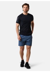 Svart atletisk t-shirt med korta ärmar, kombinerad med blå shorts och svarta sneakers. Har en reflexdetalj på ärmen.