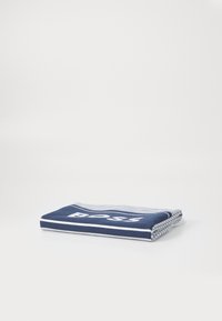 Mørkeblå håndkle med hvite striper og logo, laget av mykt stoff. Bøyd pent for å vise tekstur og design detaljer.