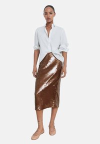 Chemise blanche à boutons, rentrée dans une jupe en sequins bronze de longueur genou avec une silhouette ajustée, accompagnée de chaussures légères à lacets.