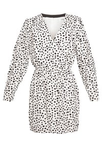 Robe enveloppante blanche avec de grands pois noirs, manches bouffantes longues, taille élastique et décolleté en V profond. Fermeture éclair au dos.