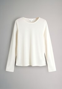 Ilga balta palaidinė su apvaliu kaklu, pagaminta iš minkštos medžiagos, su tiesiu apdailu ir šoninėmis plyšėmis, kad būtų patogiau judėti.