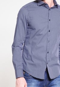 Blå och vit rutig skjorta med långa ärmar, knäppkrage och normal passform. Har en subtilt strukturerad tygkvalitet och knäppning fram.