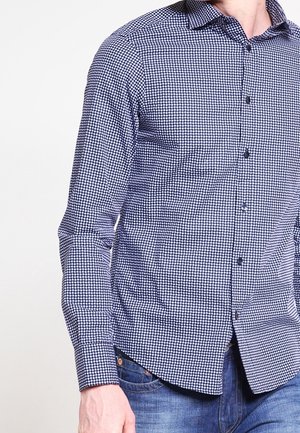 Camicia a quadratini blu e bianchi con maniche lunghe, colletto button-down e vestibilità regolare. Presenta un tessuto leggermente testurizzato e chiusura con bottoni.