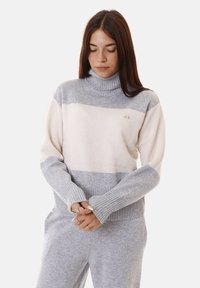 Maglione a collo alto a righe grigio chiaro e crema con polsini e orlo a coste, contraddistinto da un piccolo logo sul petto. Materiale a maglia morbido e testurizzato.