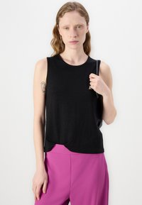 Zwarte mouwloze top met een ronde hals en een losse, gedrapeerde fit, gecombineerd met felle roze broek. De stof lijkt soepel en lichtgewicht te zijn.