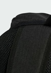 Musta reppu, jossa on tekstuurilla varustettu verkko-osa, sileä kangas ja vahvistetut saumat. Varustettu pehmustetuilla hihnoilla ja minimalistisella muotoilulla.