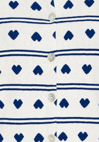 Cárdigan blanco con un patrón repetido de corazones azules y franjas horizontales en azul marino. Abrochado con botones redondos de color claro.