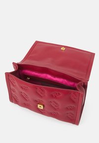 Borsa in pelle rossa con design del logo in rilievo, hardware dorato e un interno foderato di rosa con una tasca con zip. Aperta, senza manici visibili.