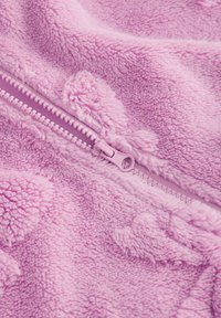 Tissu en polaire rose doux avec une fermeture éclair rose fermée et un motif subtil d'empreintes de pattes sur la surface texturée.