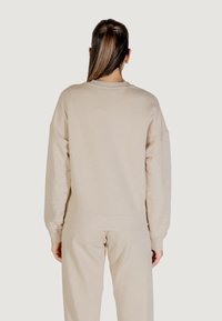 Felpa beige con una vestibilità rilassata, polsini e orlo a coste, texture morbida e design semplice, mostrata da dietro.