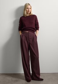 Burgunderfarbener gestrickter Pullover und weite Hosen in einer passenden tiefen Farbe, mit Frontfalten und seitlichen Taschen. Glatte Textur, taillierte Passform.